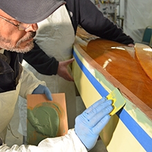 Applying TotalBoat TotalFair Epoxy Fairing Compound to even out the surface on a wooden kayak.