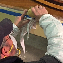 Sanding TotalBoat TotalFair Epoxy Fairing Compound on the side of a wooden kayak.